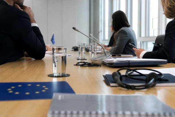 Table de négociation européenne avec dossiers, écouteurs, verres d’eau et petits drapeaux discrets