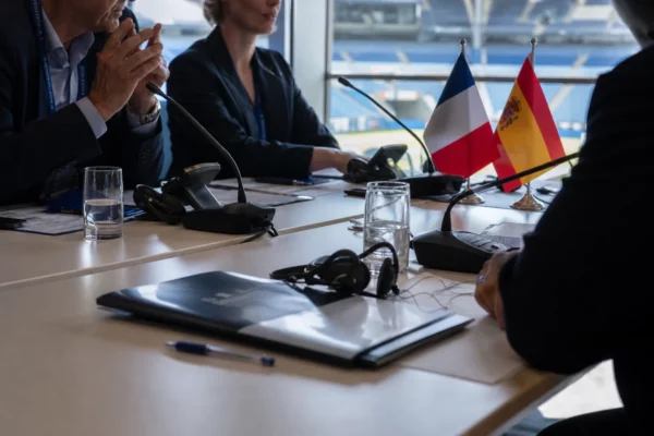 Table de négociation internationale avec dossiers, micros et mini-drapeaux France-Espagne dans une salle lumineuse.
