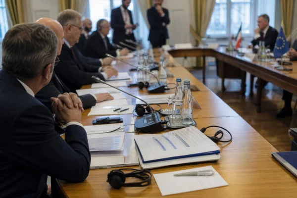Table de négociation internationale avec dossiers, micros et silhouettes anonymes dans une salle lumineuse.