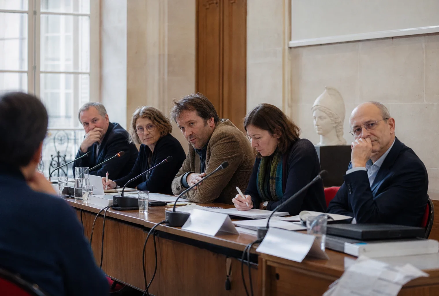 Table ronde d’universitaires à Paris, avec micros et dossiers flous dans une salle institutionnelle lumineuse.