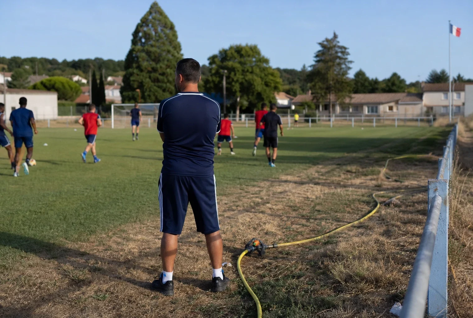 Terrain de football municipal en France avec un entraînement ordinaire et un arrosage au bord de la pelouse
