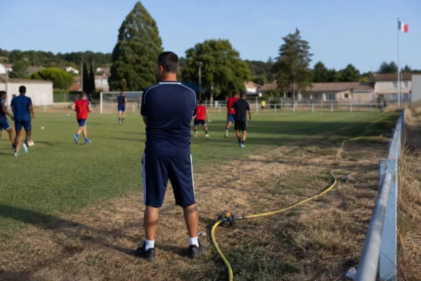 Terrain de football municipal en France avec un entraînement ordinaire et un arrosage au bord de la pelouse