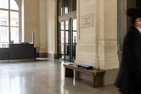 Entrée d’un palais de justice parisien, lumière naturelle claire et dossier juridique discret sur un banc.