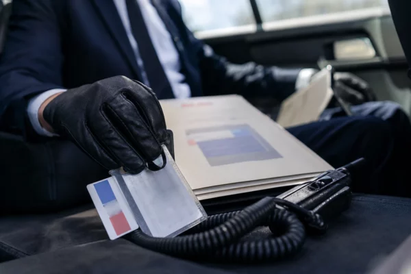 Gros plan photojournalistique sur un badge, un dossier et une radio dans l’habitacle d’une voiture officielle électrique.