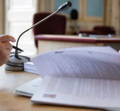 Mains anonymes examinant un dossier d’audition près d’un micro de commission dans une salle institutionnelle française