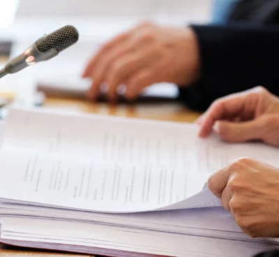 Mains anonymes examinant un dossier juridique près d’un micro de commission dans une salle institutionnelle française