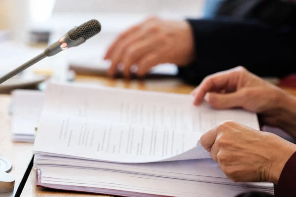 Mains anonymes examinant un dossier juridique près d’un micro de commission dans une salle institutionnelle française