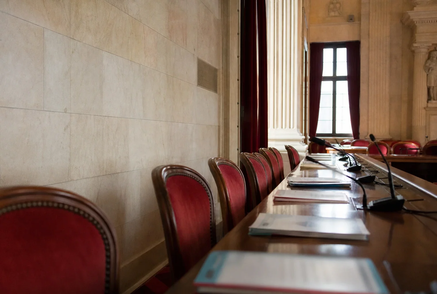 Salle parlementaire française vide avec sièges rouges et micros, évoquant le débat sur l’alliance des écologistes