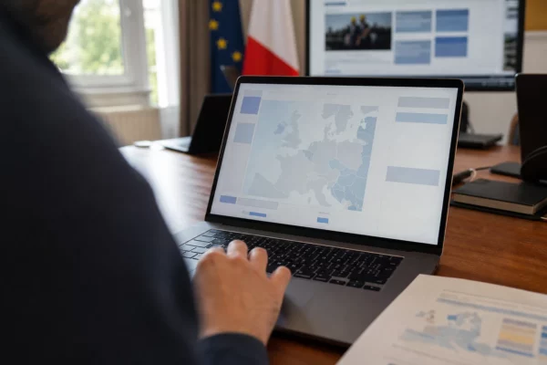 Journaliste anonyme devant un ordinateur affichant une interface européenne abstraite dans un bureau politique français lumineux.