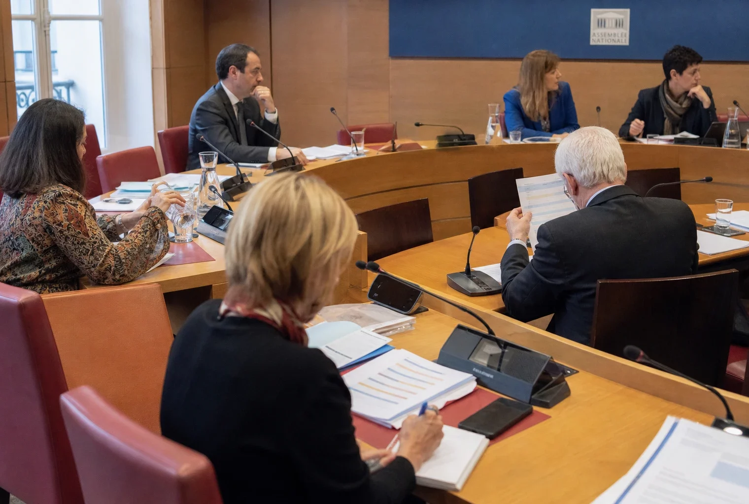 Réunion de commission parlementaire française sur le budget, avec élus anonymes, micros et dossiers sur les tables
