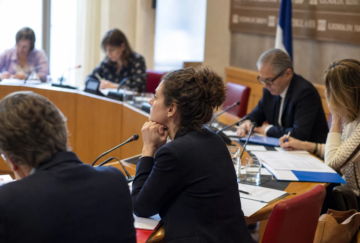 Réunion de commission française avec élus anonymes, micros et dossiers ouverts autour d’une table claire