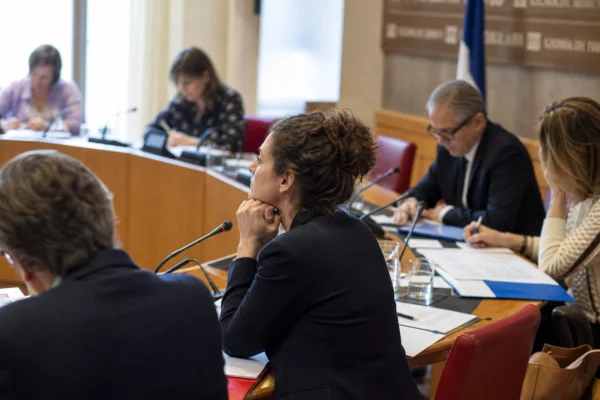 Réunion de commission française avec élus anonymes, micros et dossiers ouverts autour d’une table claire