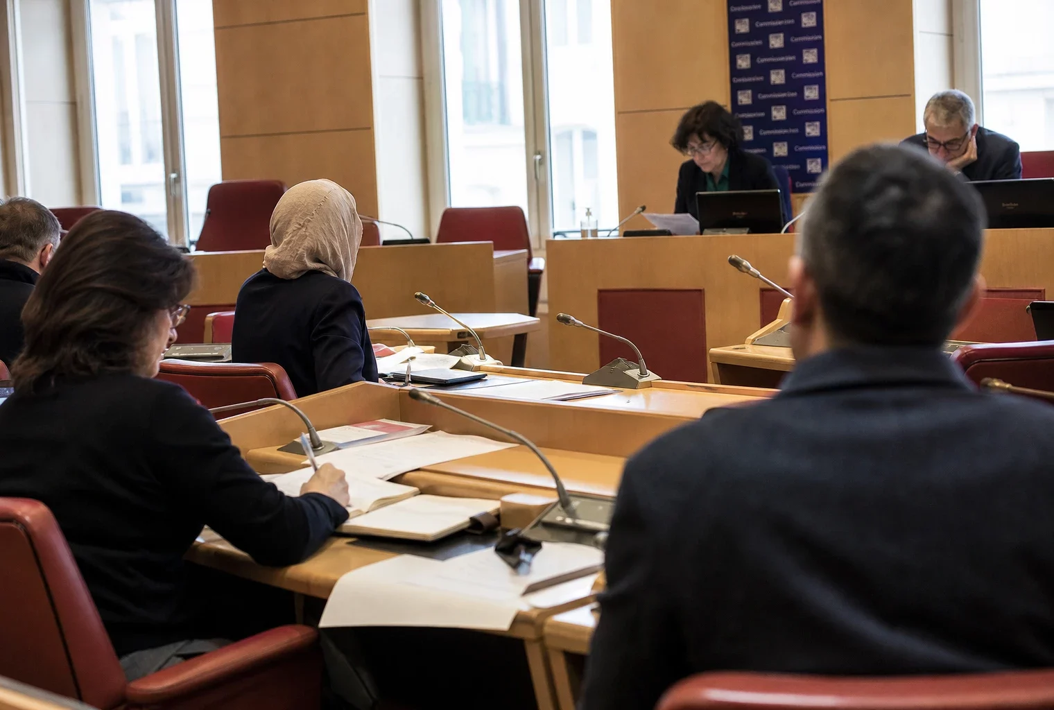 Réunion de commission parlementaire française avec une femme voilée, des micros et des dossiers anonymes