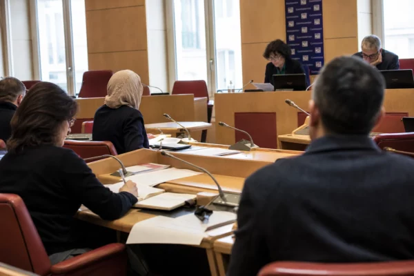 Réunion de commission parlementaire française avec une femme voilée, des micros et des dossiers anonymes