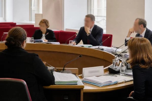 Réunion de commission parlementaire avec micros, dossiers et silhouettes anonymes dans une salle baignée de lumière naturelle.