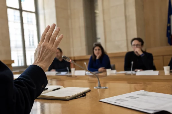 Salle publique française avec une main levée, un micro et un document juridique flou lors d’un débat démocratique