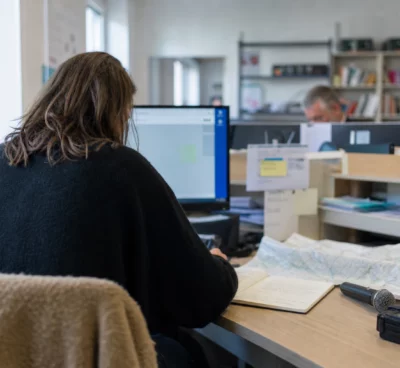 Journaliste préparant un sujet local dans une rédaction, avec carnet, carte floue et micro de presse sans logo