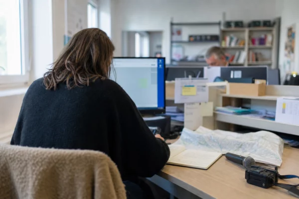 Journaliste préparant un sujet local dans une rédaction, avec carnet, carte floue et micro de presse sans logo
