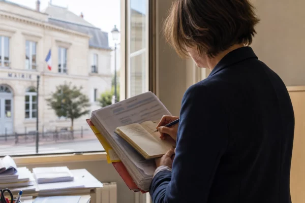 Élu local anonyme annotant un dossier budgétaire dans une mairie française lumineuse