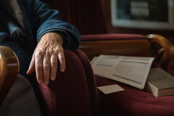 Main posée sur un fauteuil de salle culturelle près d’un billet et d’un programme flou, illustration des choix budgétaires sociaux
