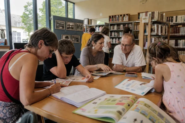Visiteurs anonymes feuilletant des cahiers de vacances dans une médiathèque municipale française lumineuse