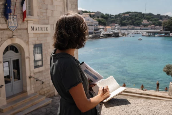 Élu local anonyme prenant des notes face à la mer chaude depuis une mairie méditerranéenne