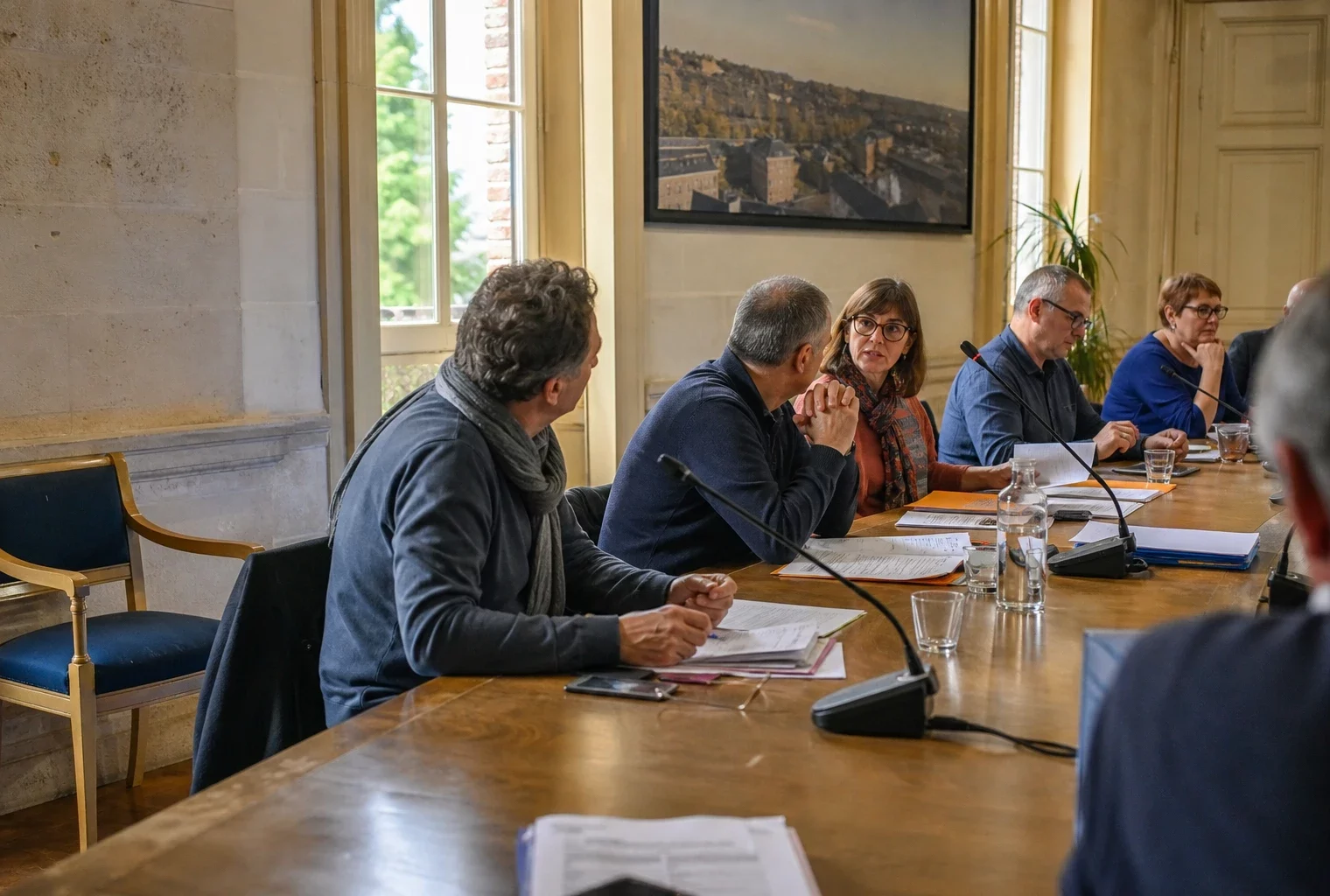 Conseil municipal français avec micros, dossiers et une chaise vide, symbole d’un débat sur le chômage des jeunes