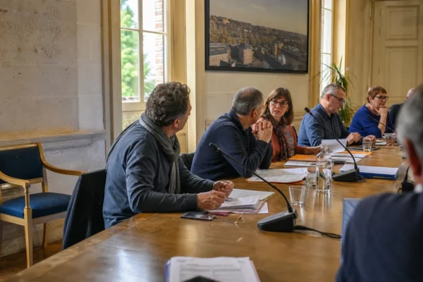 Conseil municipal français avec micros, dossiers et une chaise vide, symbole d’un débat sur le chômage des jeunes