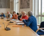 Salle de conseil municipal française avec micros, dossiers flous et une chaise vide, illustrant les échanges commerciaux UE-États-Unis