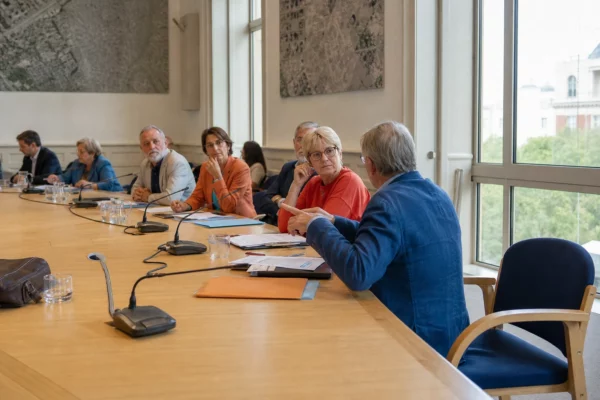 Salle de conseil municipal française avec micros, dossiers flous et une chaise vide, illustrant les échanges commerciaux UE-États-Unis