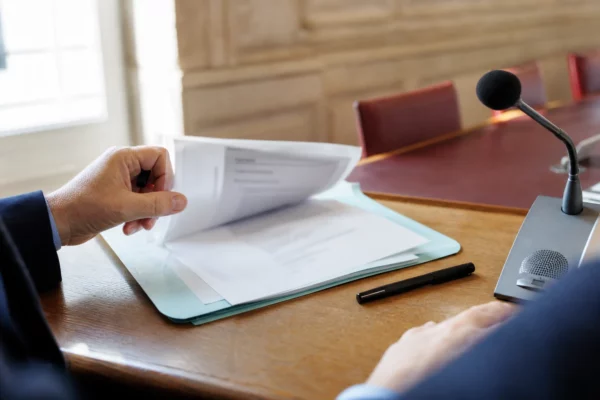 Mains anonymes examinant un dossier flou près d’un micro de commission dans une salle parlementaire française