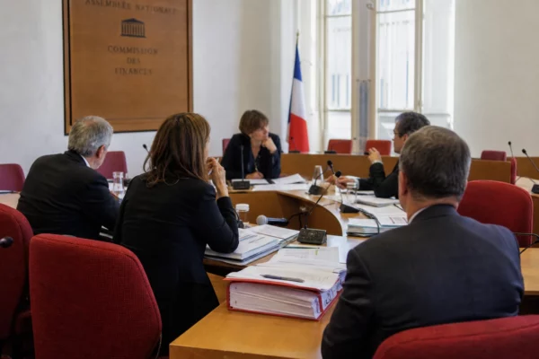 Réunion de commission parlementaire avec micros, dossiers ouverts et silhouettes anonymes dans une salle lumineuse