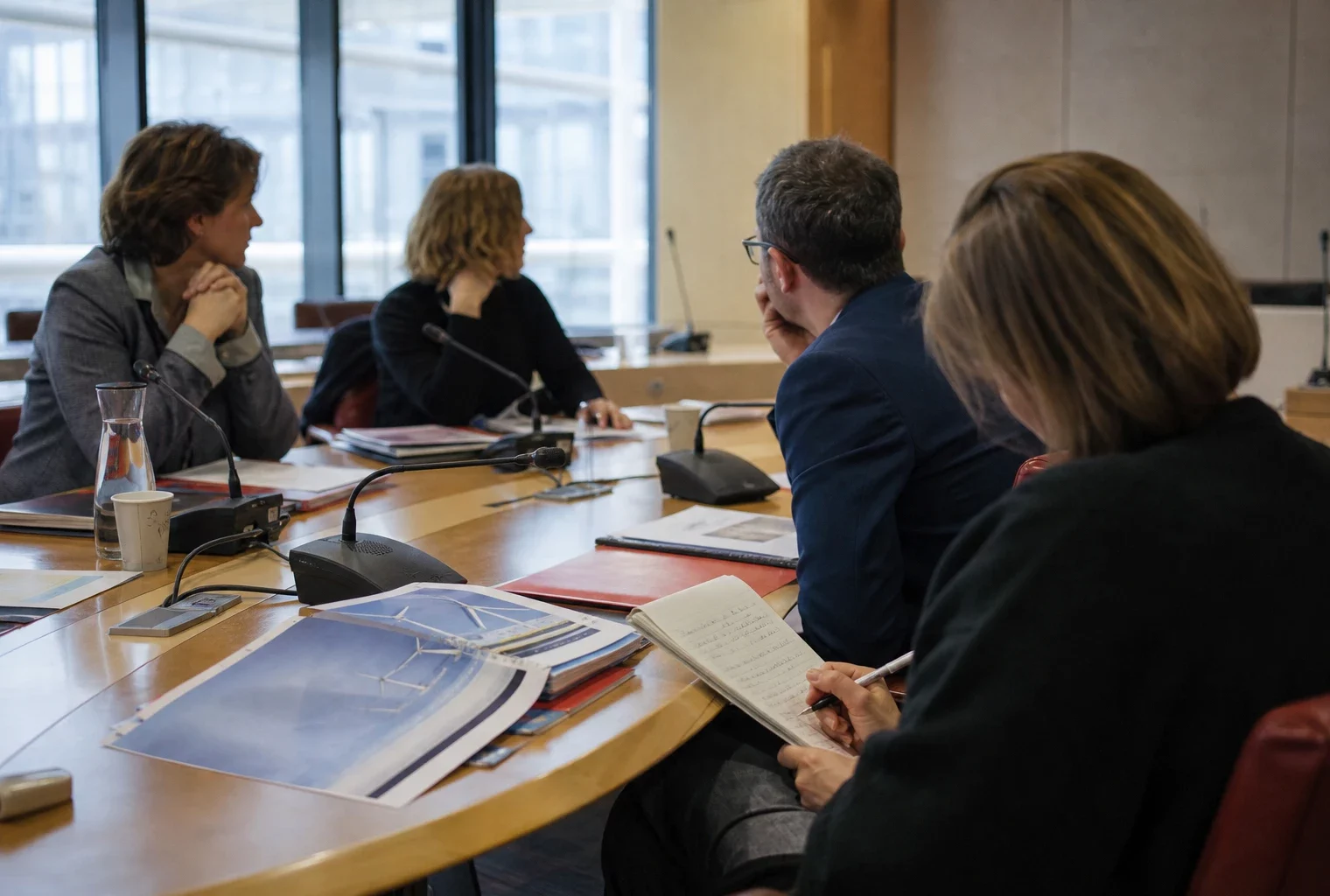 Réunion de commission parlementaire sur l’énergie, avec micros, dossiers et participants anonymes dans une salle claire