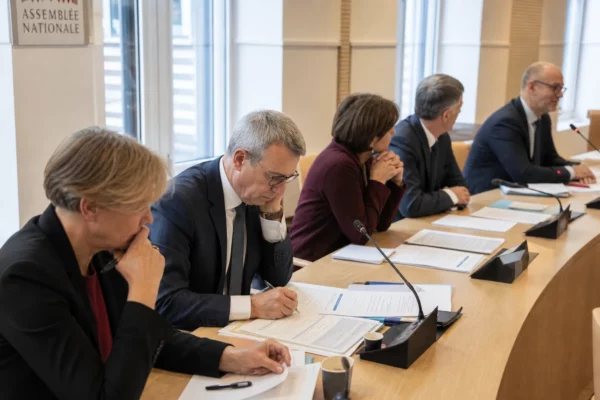Réunion de commission parlementaire française avec des fonctionnaires anonymes, micros et dossiers sur la table