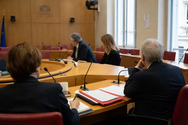 Réunion de commission parlementaire avec des hauts fonctionnaires anonymes, micros et dossiers sur la table