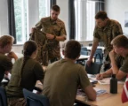 Briefing militaire au Danemark avec plusieurs conscrits réunis autour d’une table dans une salle lumineuse.