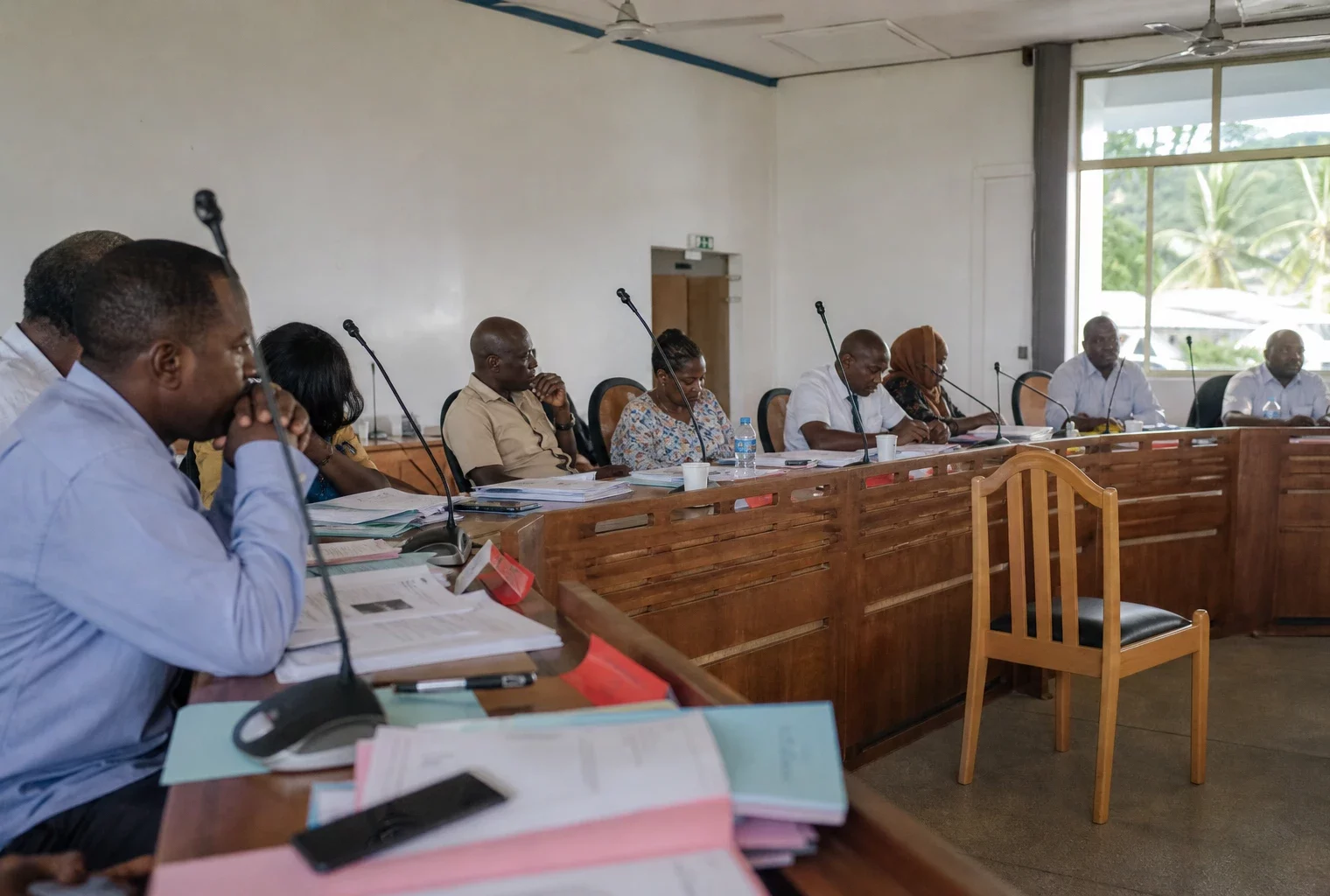 Salle de conseil local à Mayotte avec une chaise vide, des micros et des dossiers lors d’un débat public
