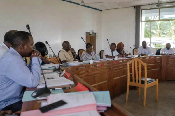 Salle de conseil local à Mayotte avec une chaise vide, des micros et des dossiers lors d’un débat public