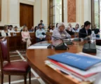 Salle municipale lumineuse avec micros et dossier flous, autour d’une chaise vide au premier plan