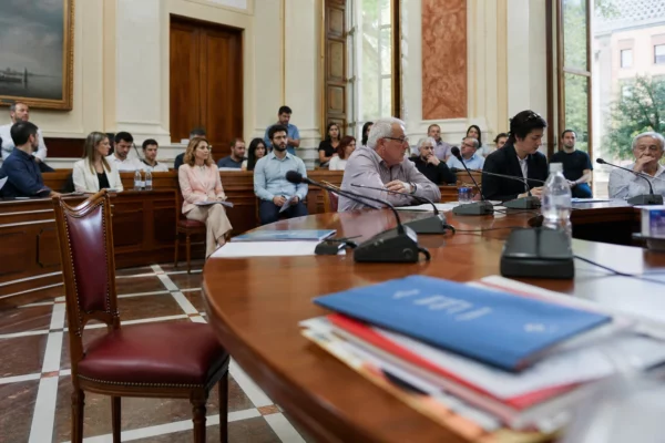 Salle municipale lumineuse avec micros et dossier flous, autour d’une chaise vide au premier plan