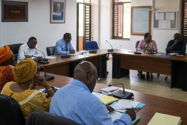 Salle municipale à Mayotte avec élus locaux, micros et chaise vide lors d’une réunion sur la reconstruction