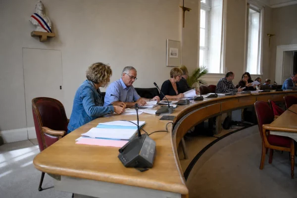 Salle municipale française avec élus anonymes, chaise vide, micros et dossiers lors d’un conseil local