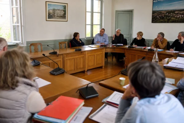 Salle de conseil municipal française avec chaise vide, micros et dossiers flous pour illustrer un sondage électoral