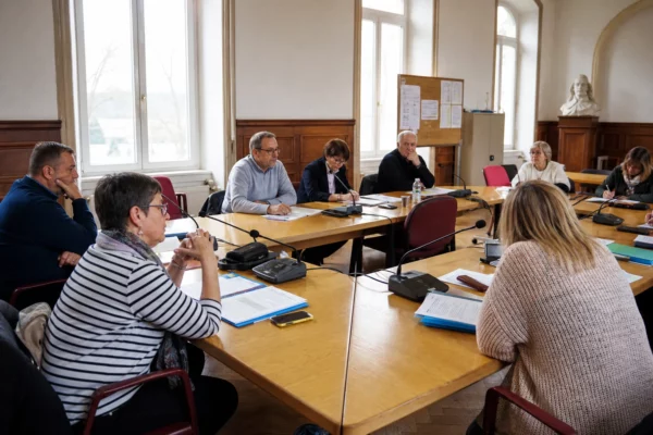 Conseil municipal français discutant des services publics autour de micros, dossiers flous et d’une chaise vide