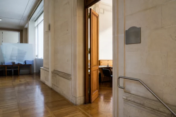 Couloir lumineux d’un bâtiment institutionnel français menant à une salle d’audition, ambiance sobre et documentaire.