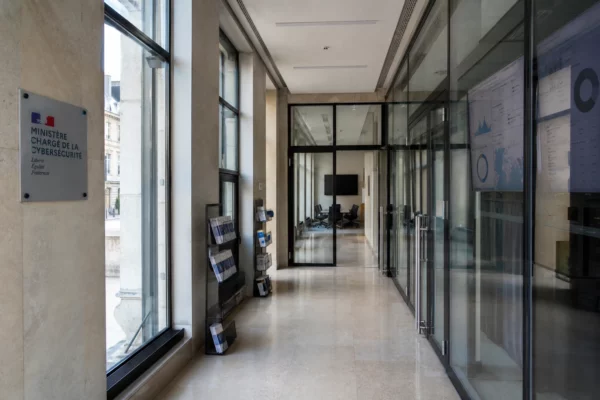 Couloir vide d’un bâtiment institutionnel parisien, lumière naturelle claire et ambiance de vigilance démocratique.