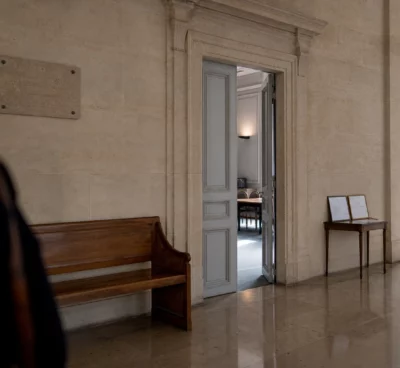 Couloir lumineux d’une institution française, porte entrouverte et salle d’audition visible au fond.