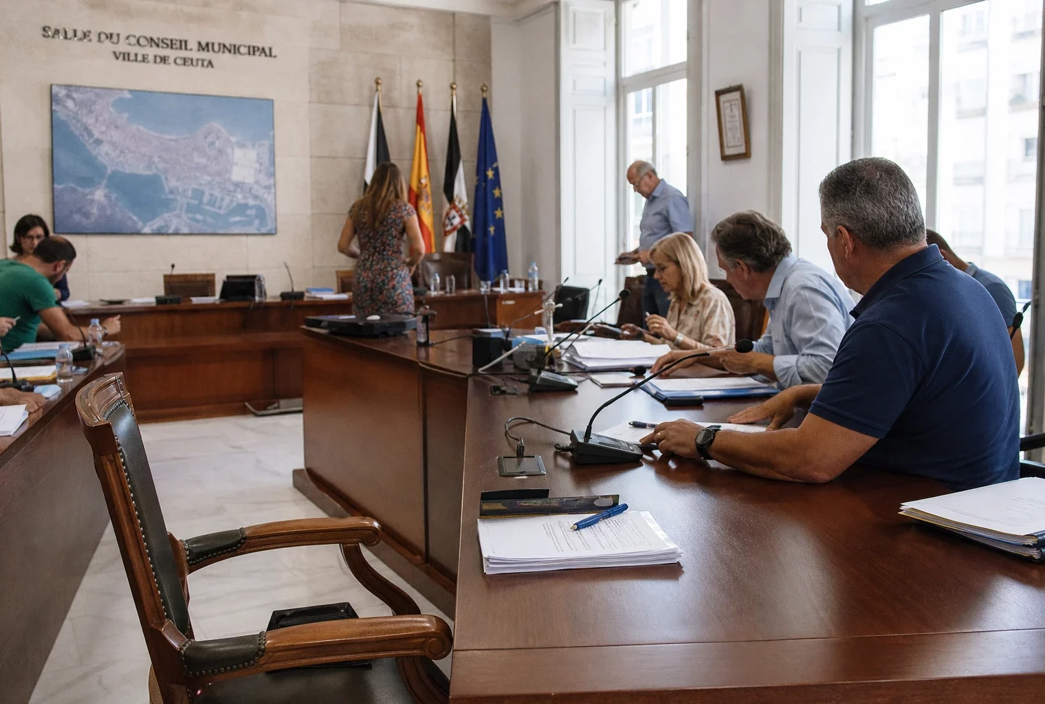 Salle municipale de Ceuta après une crise migratoire, avec chaise vide, micros et dossiers sur une table