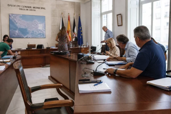 Salle municipale de Ceuta après une crise migratoire, avec chaise vide, micros et dossiers sur une table