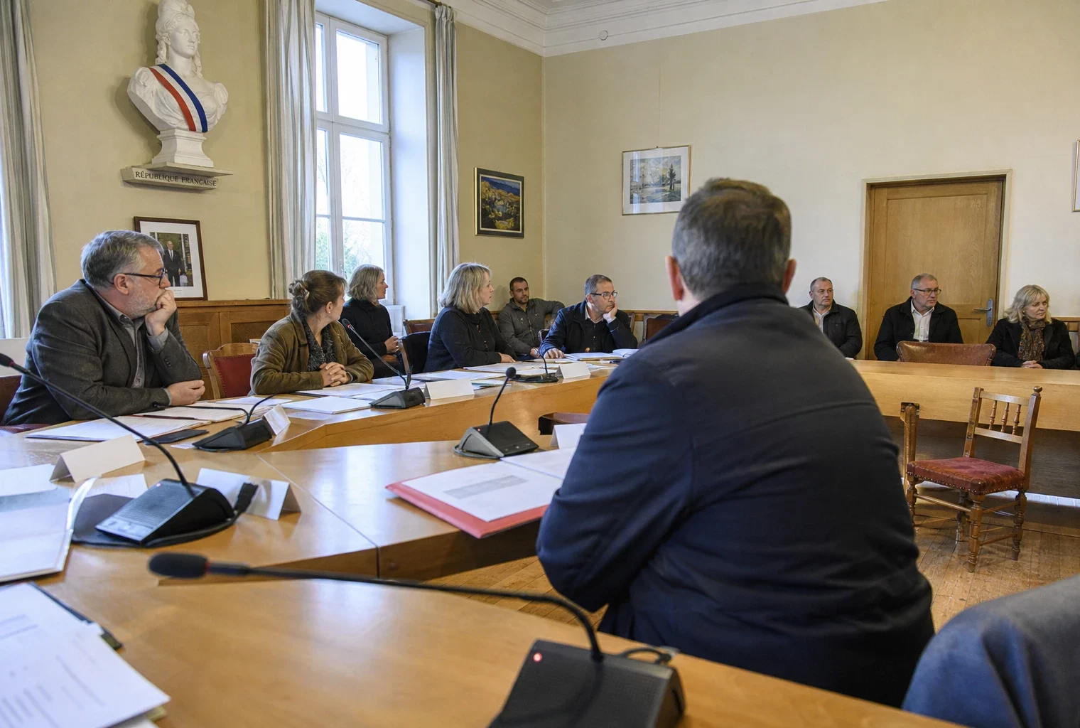 Salle de conseil municipal française avec une chaise vide, des micros et des dossiers lors d’une réunion publique